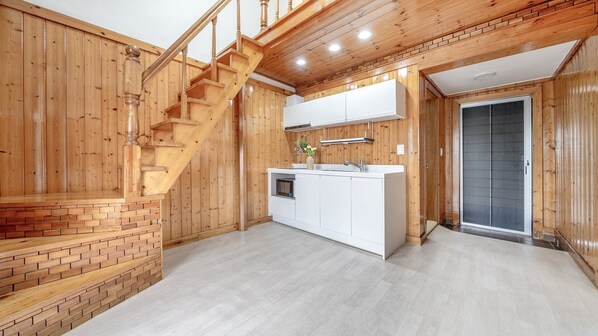 A kitchen with wooden walls, a brick accent wall, and a wooden staircase.