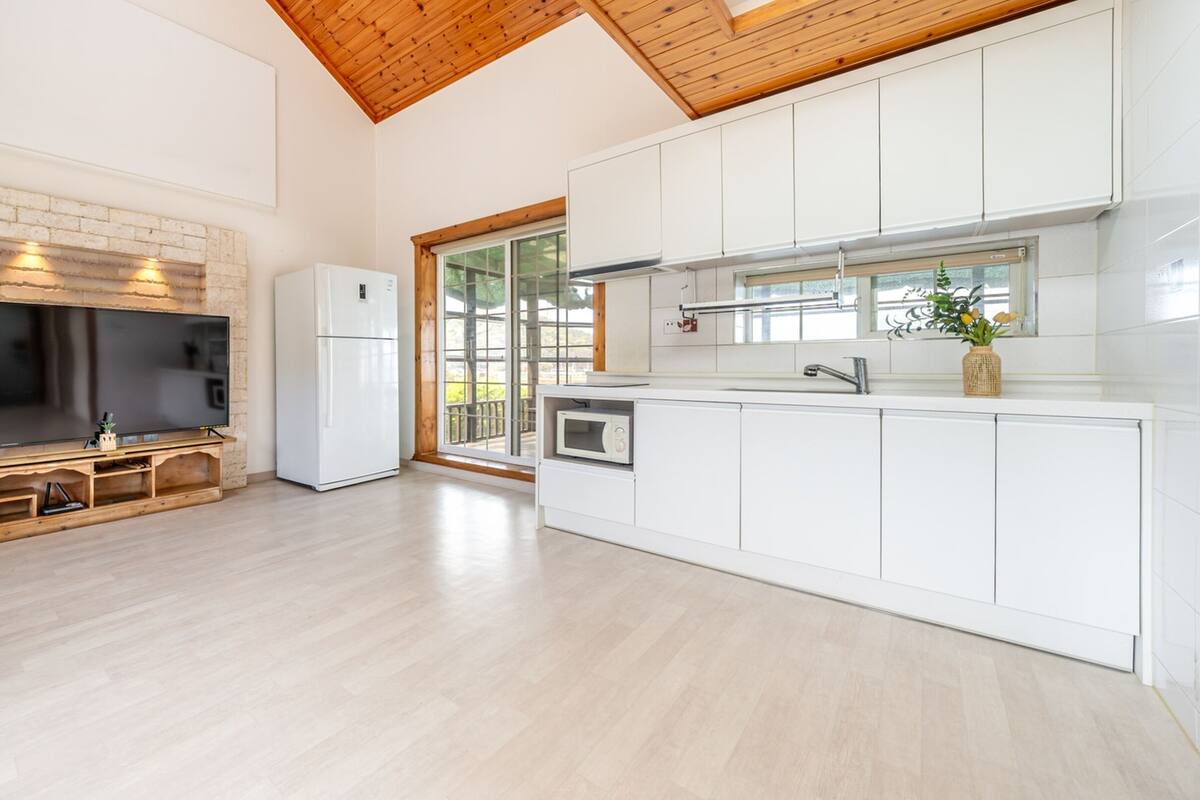 A modern kitchen with white cabinetry, a built-in microwave, and a large TV.