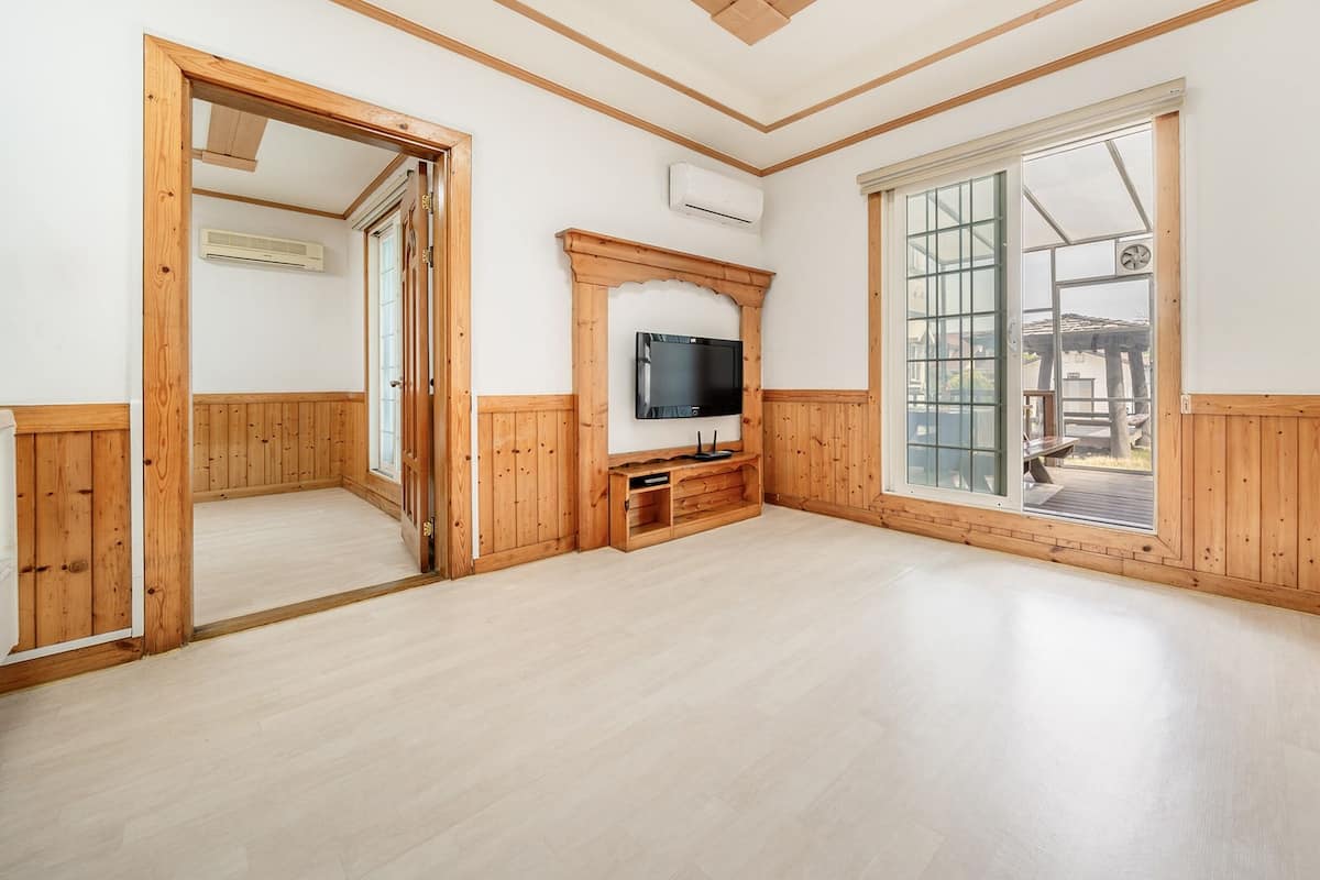 A spacious room with wooden paneling, a large window with a view of an outdoor deck, and a built-in entertainment unit.