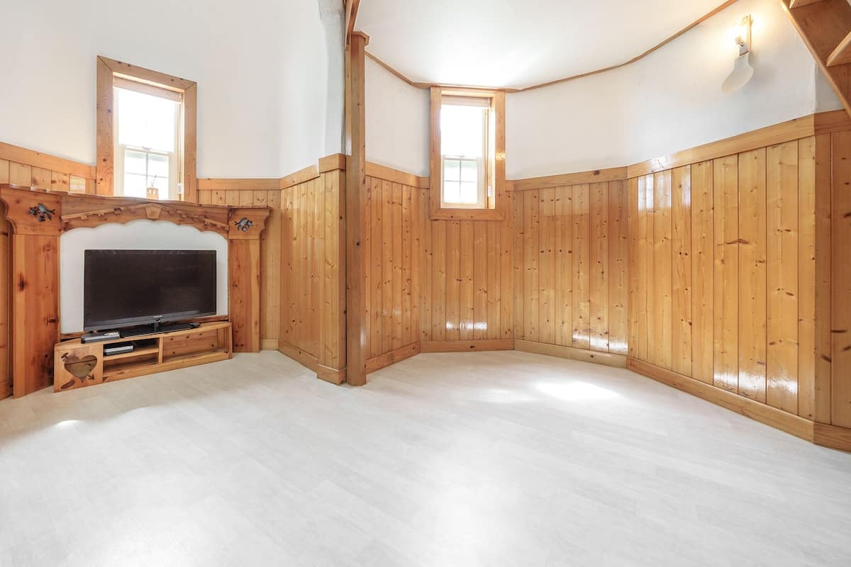 A room with wooden paneling, a large flat-screen TV, and two windows.