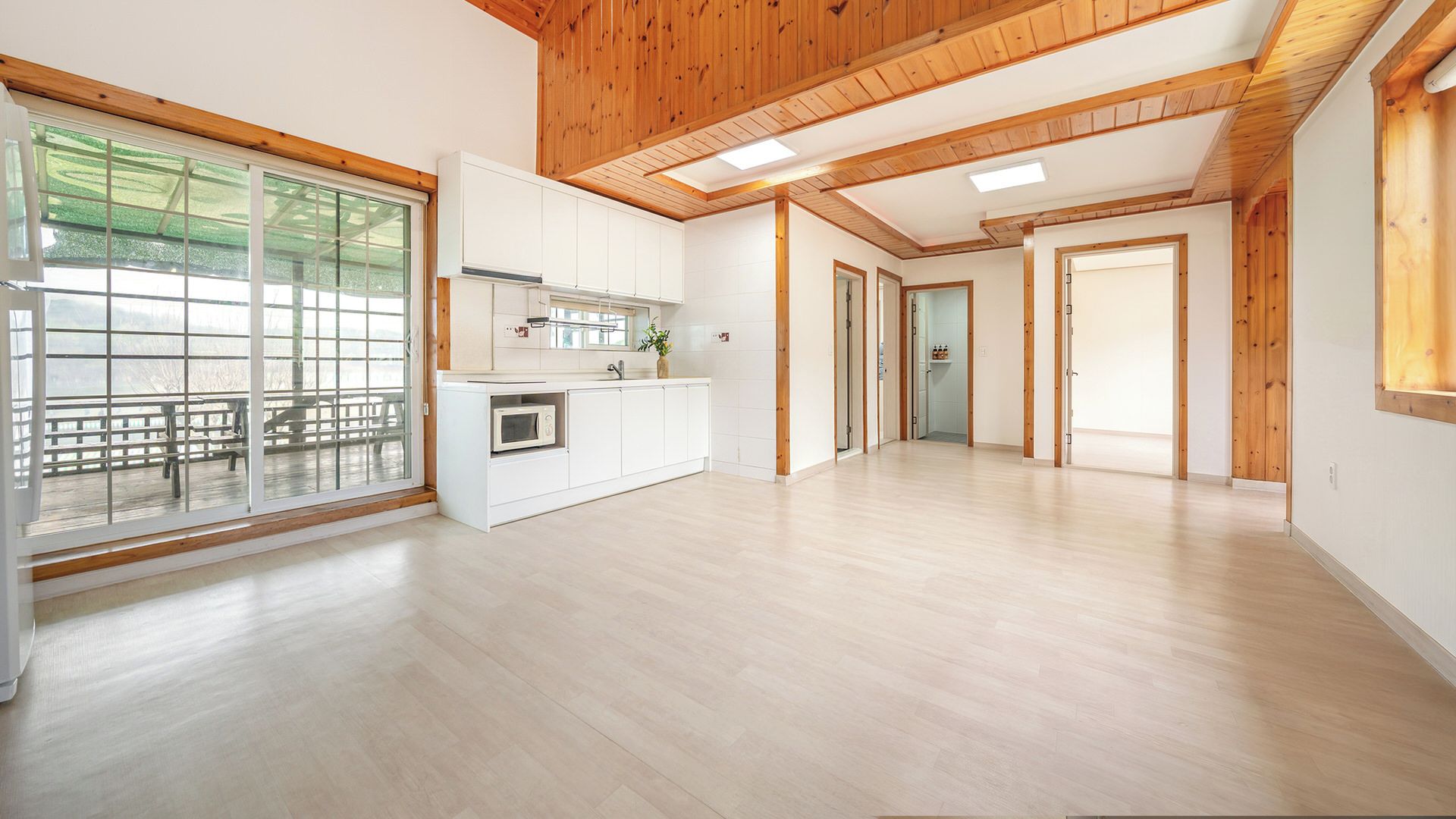 Ein geräumiges Zimmer mit Holzbalkendecke, einem großen Fenster und einer Küchenzeile.