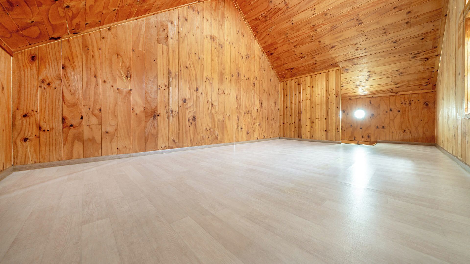 Een ruime zolderkamer met houten wanden en een schuin plafond.
