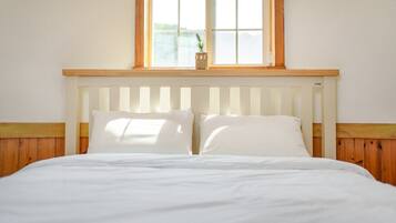 A bed with white bedding, a wooden headboard, and a window above.