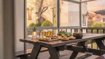 A wooden table with a variety of food and drinks, a lantern, and a view of buildings through large windows.