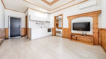 Una habitación amplia con kitchenette, televisor y puerta que da a otra habitación.