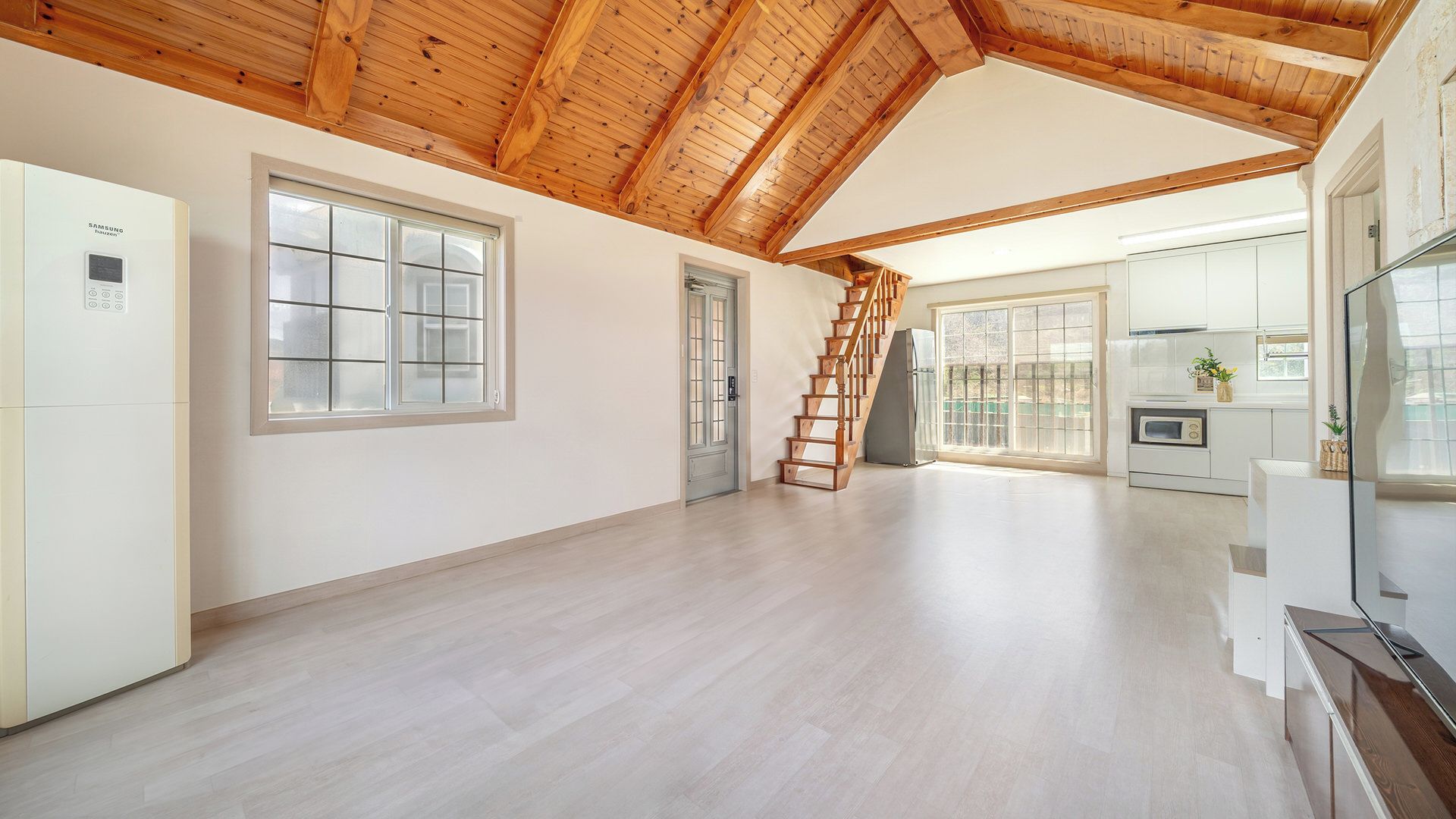 A spacious room with a wooden ceiling, a staircase, and a kitchen area.