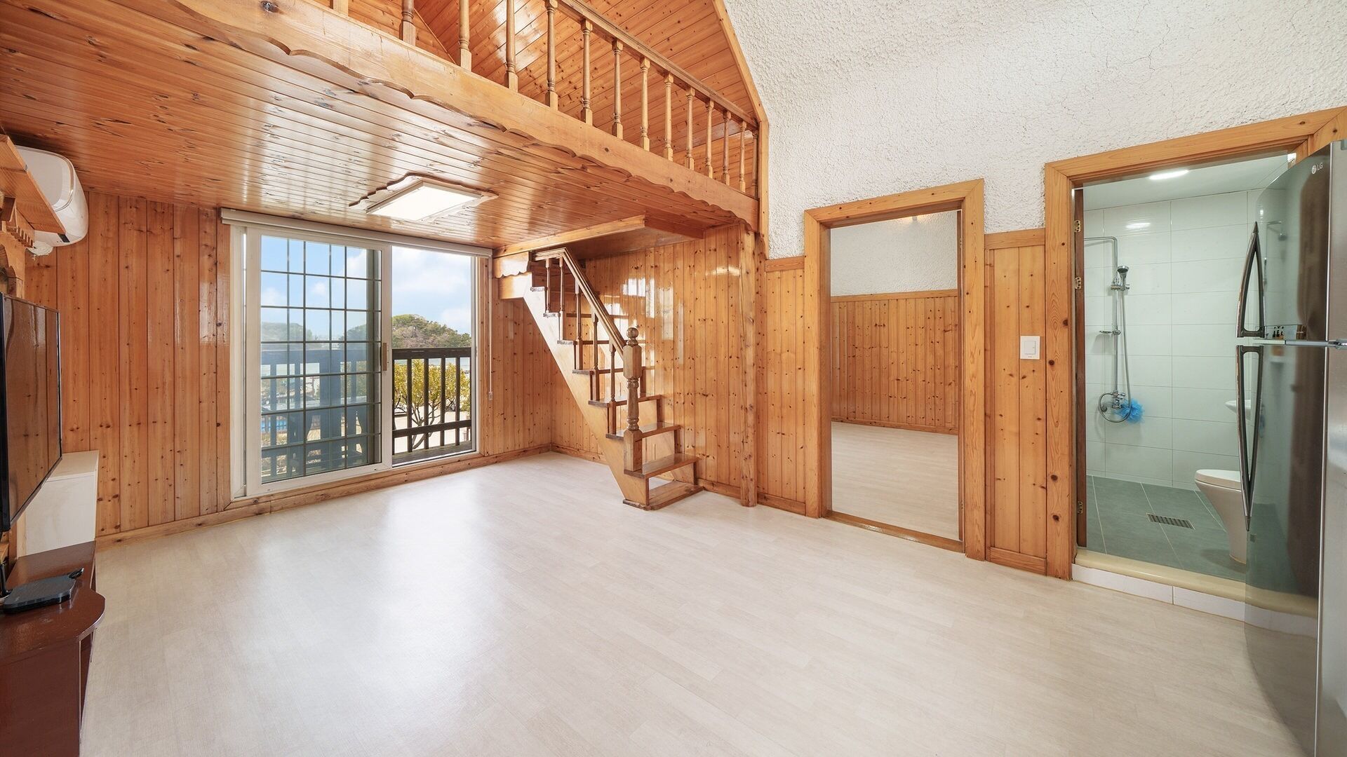 A spacious room with a wooden staircase, a glass shower enclosure, and a large sliding glass door leading to an outdoor area.