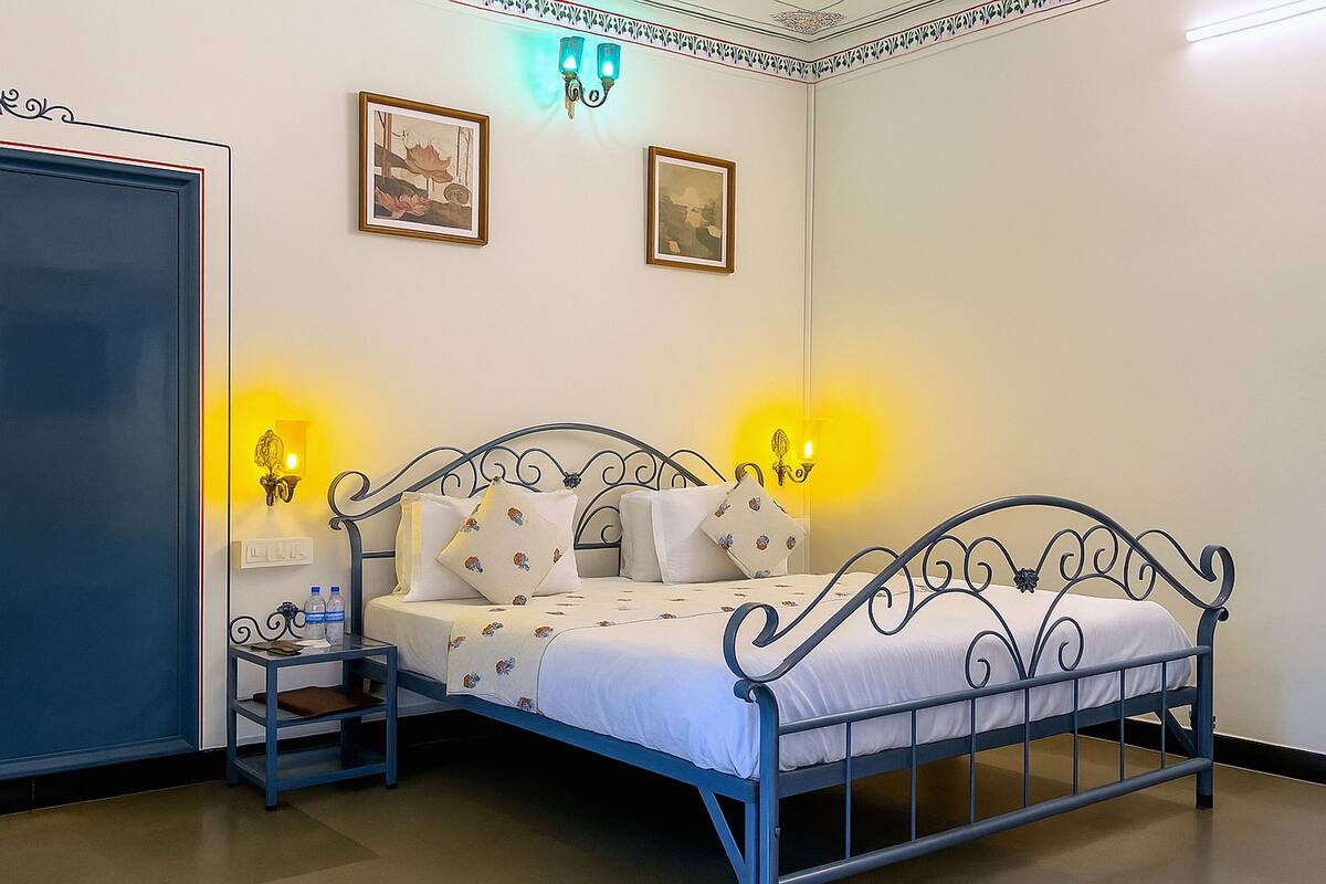 A bedroom with a metal bed frame, white bedding, two wall-mounted lamps, and framed pictures on the wall.
