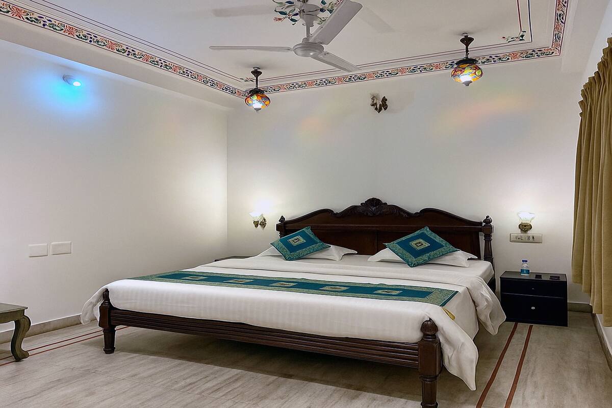 A neatly made bed with a wooden headboard, two wall sconces, a ceiling fan, and a small bedside table with a bottle.