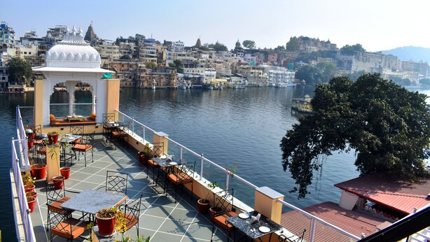 A terrace with outdoor seating overlooking a river, surrounded by buildings. - Hotel Thamla Haveli (Udaipur)