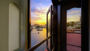 A view through a window with a metal railing, overlooking a calm body of water with a bridge and buildings in the distance. - Hotel Thamla Haveli (Udaipur)