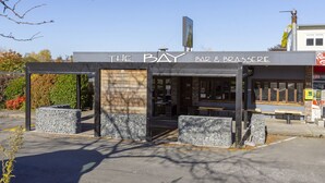Een bar en bistro genaamd "The Bay" met een modern design, terras en een helder uitzicht op de straat.