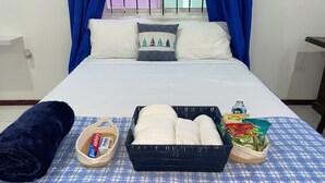 Un lit bien fait, recouvert d’une couverture à carreaux bleus et blancs, un panier noir contenant des objets blancs, un oreiller bleu et une couverture bleue posés sur une nappe à carreaux.