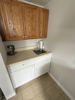 Compact kitchen with a stainless steel sink, coffee maker, and soap dispenser.