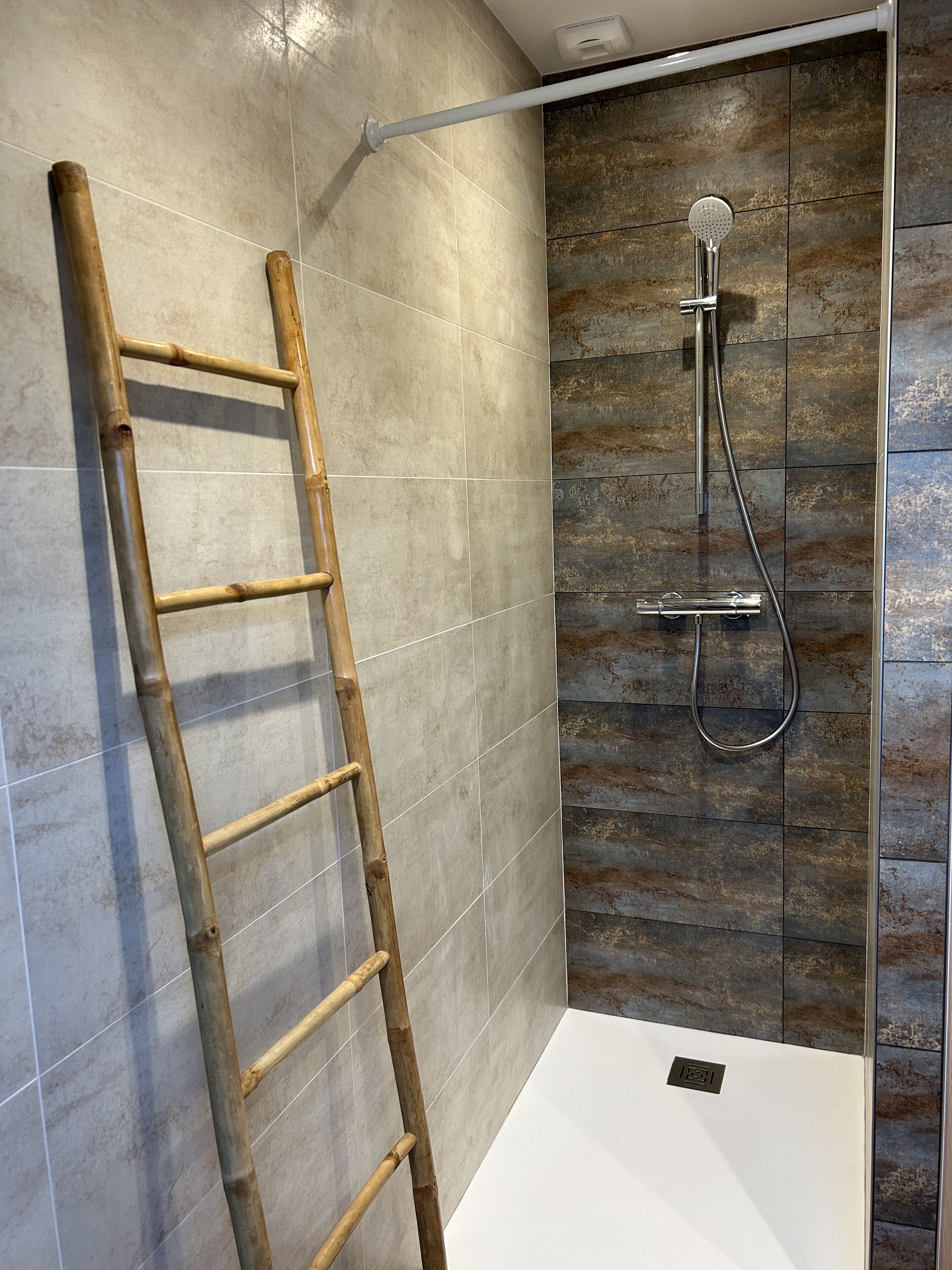 Zona de ducha con escalera de bambú, ducha de mano y panel de control en la pared.