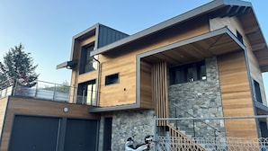 A modern two-story house with a stone facade, a wooden deck, and a motorcycle parked in front.