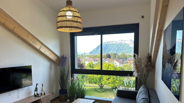A modern living room with a large window, a flat-screen TV, a sofa, and a wooden entertainment unit.