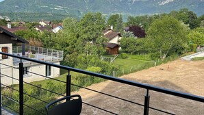A balcony with two tables and chairs, overlooking a mountainous landscape with houses and greenery.