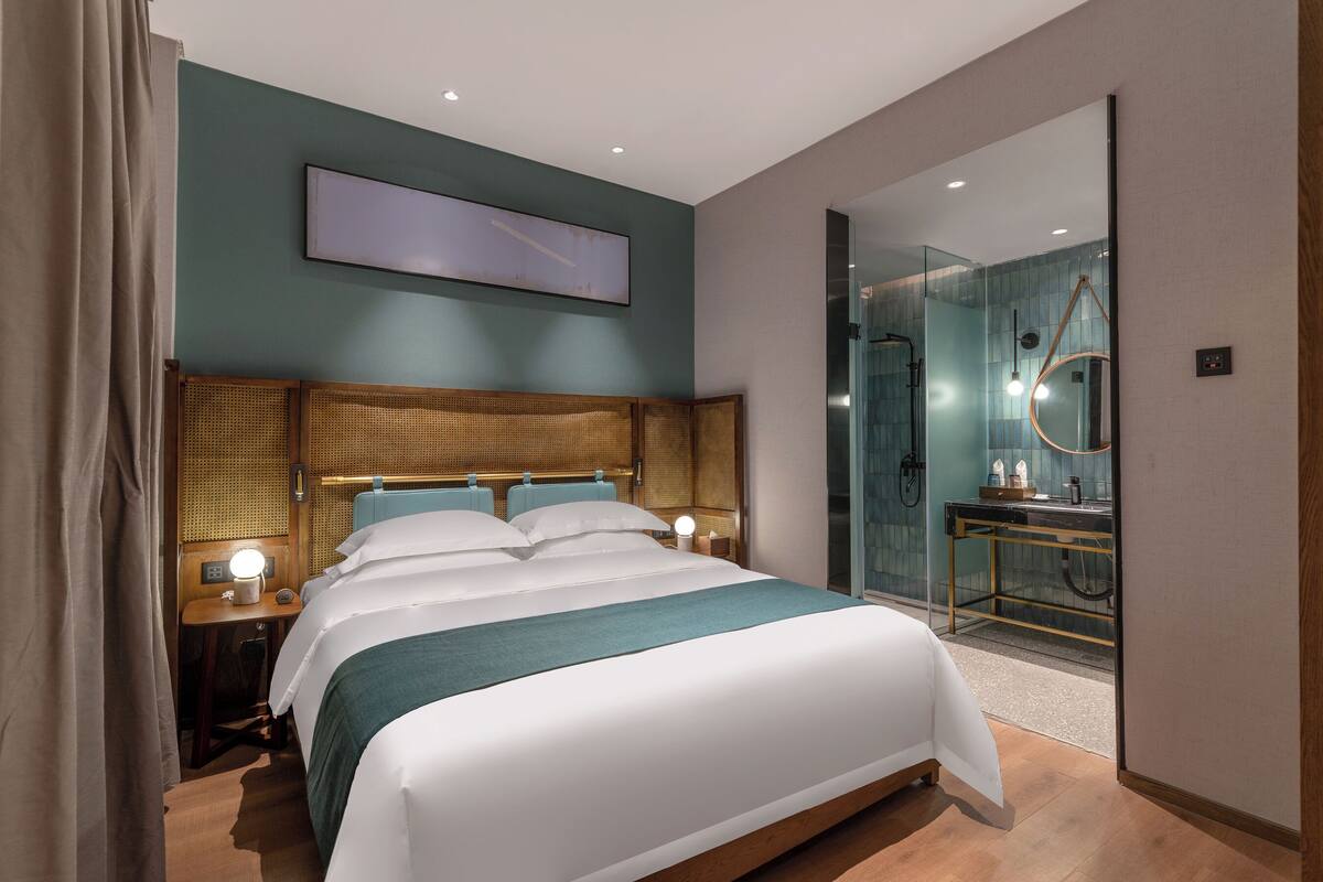A modern hotel room with a large bed, bedside lamps, a mirror, and a glass shower enclosure.