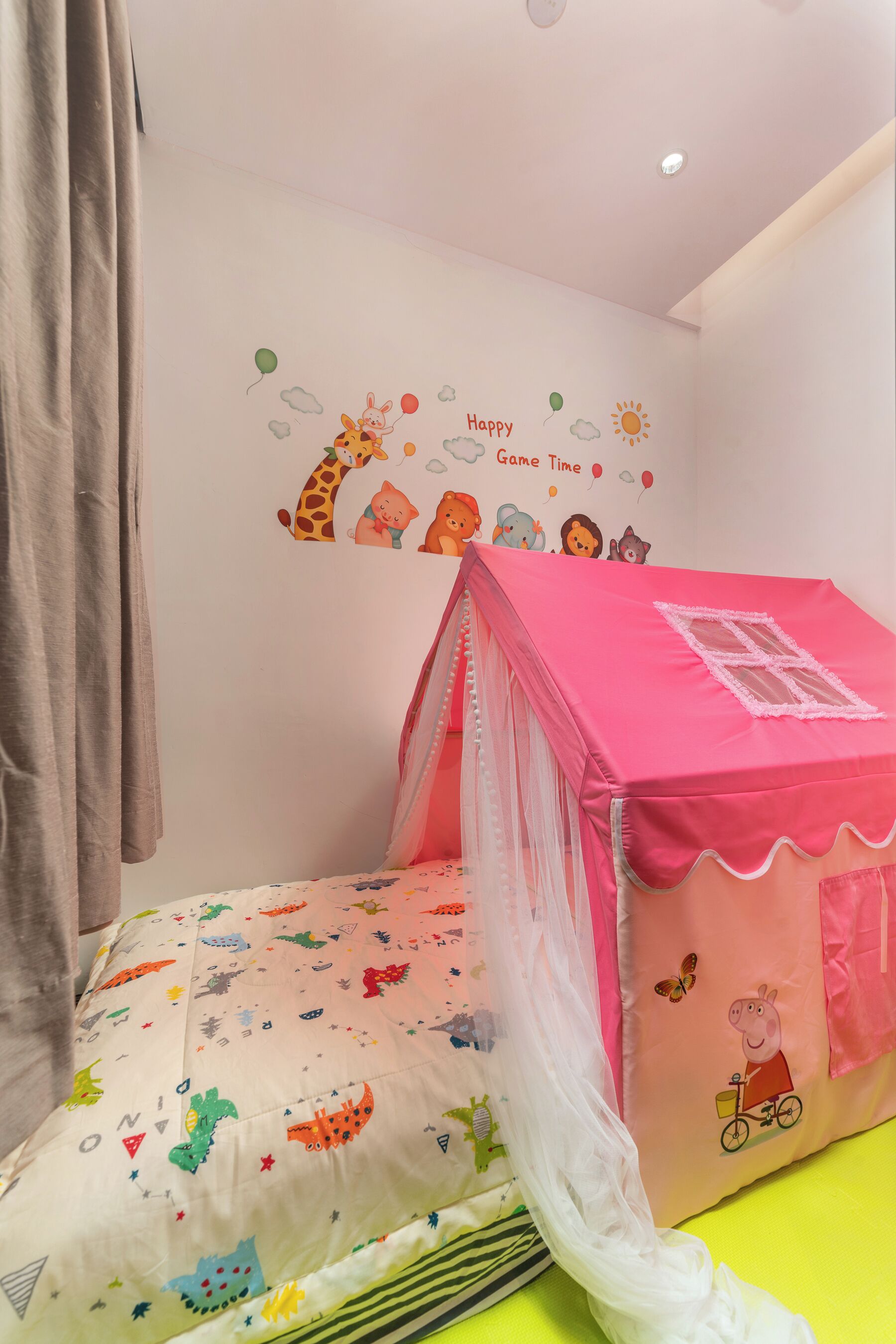 Une chambre d’enfant avec une maisonnette rose, un lit recouvert d’une couette aux motifs colorés d’animaux, et un mur décoré d’autocollants d’animaux et de l’inscription « Amusez-vous bien ! ».