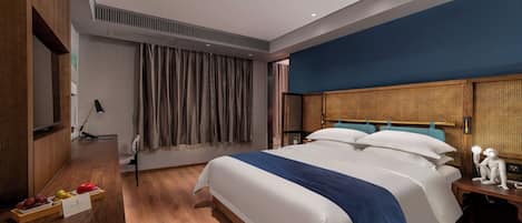 Habitación de hotel moderna con una cama grande, suelo de madera, un escritorio con lámpara y una mesita con un objeto decorativo.