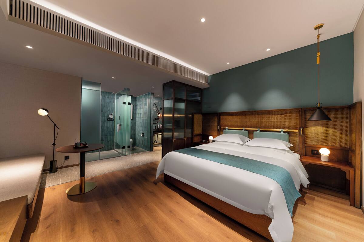 A modern hotel room with a large bed, bedside tables, a desk, and a mirror.