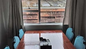 Een kamer met een grote houten tafel, twee blauwe stoelen en een raam met gordijnen.