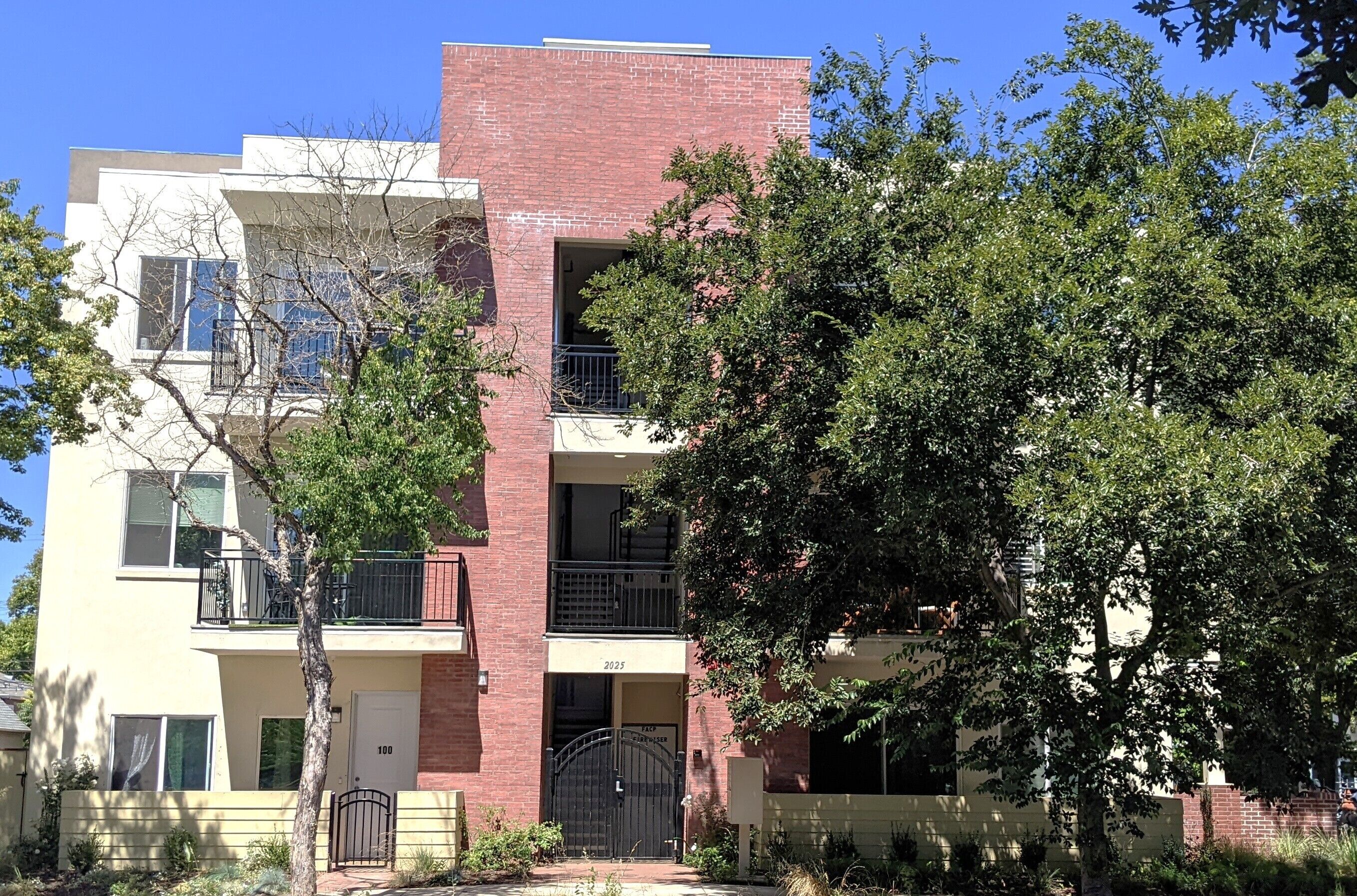 A multi-story apartment building with a brick facade, numbered units, and a gated entrance.