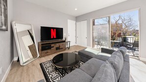 Ett modernt vardagsrum med en stor platt-TV, en soffa, ett soffbord och en skjutdörr i glas som leder ut till en uteplats.