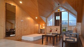 A spacious room with wooden walls and a sloped ceiling, featuring a large mirror, a bed, a dining table with chairs, and a view through a large window. - Zen Zone The Laurent and Banon  (Manali)