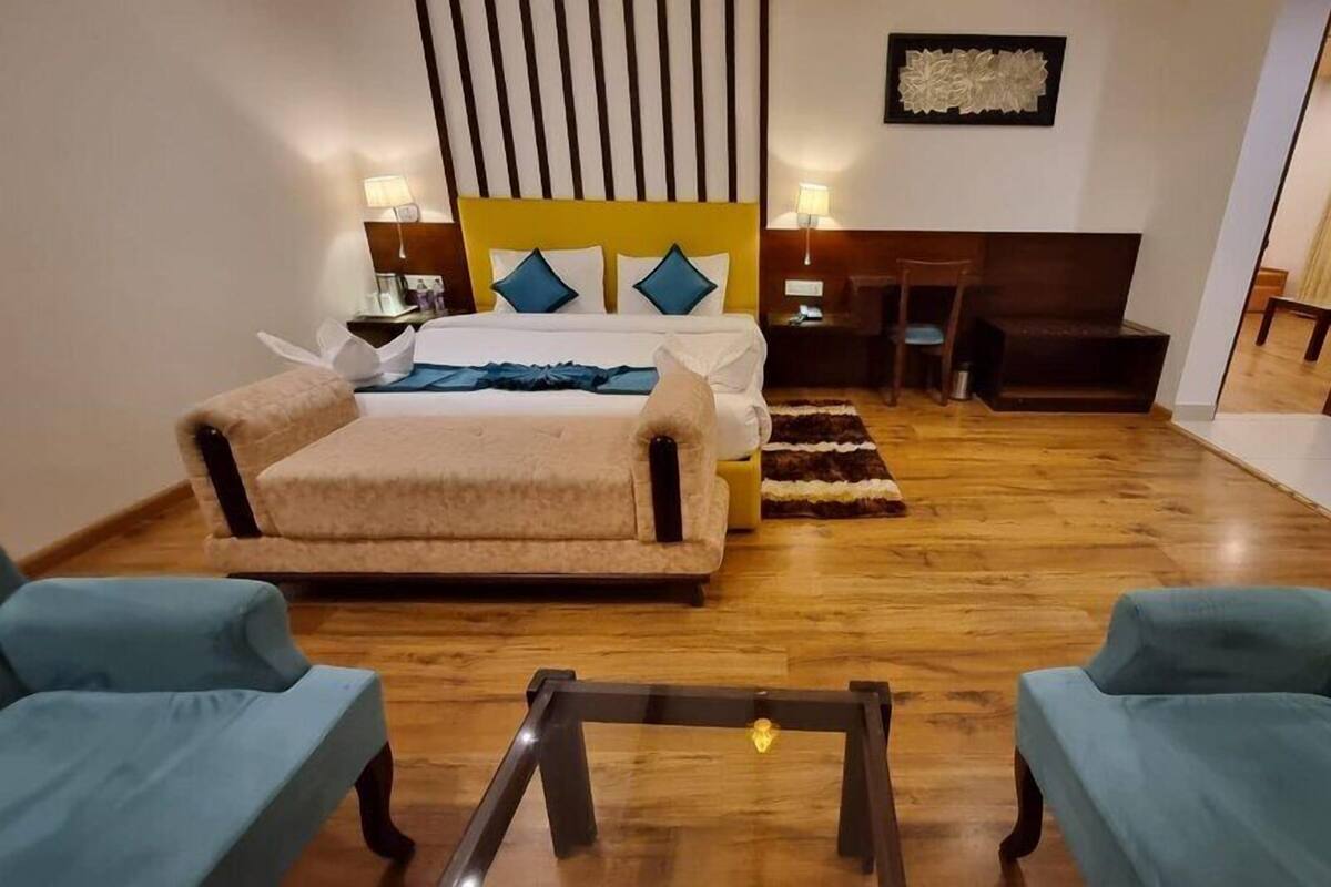 A hotel room with a large bed, two armchairs, a small table, and a desk with a chair.
