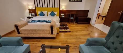 Una habitación de hotel con una cama grande, dos sillones, una mesita y un escritorio con silla.