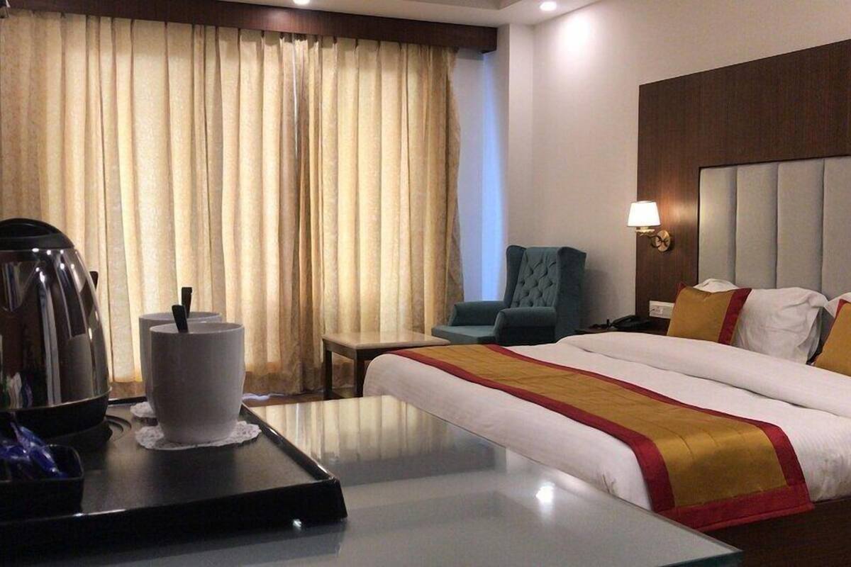 A hotel room with a bed, a chair, a table with a coffee maker, and a lamp.