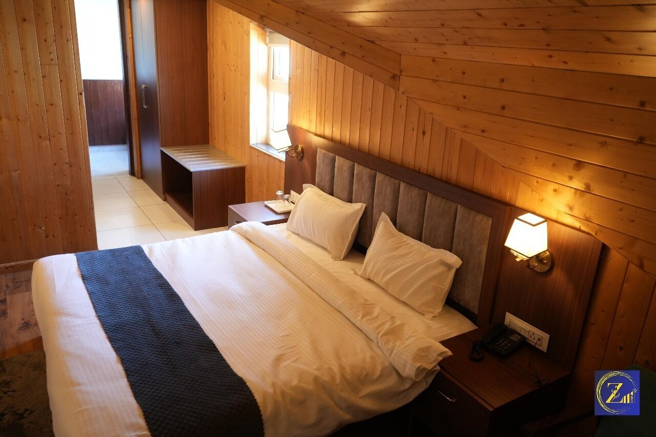A wooden-paneled room with a bed, bedside table, lamp, and a small desk.