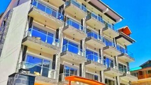 Un hôtel à plusieurs étages, doté de balcons, d’une entrée couverte et surplombant un ciel d’un bleu limpide.