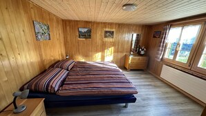 A wooden-paneled bedroom with a bed, dresser, and artwork on the walls.