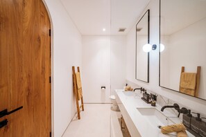 A modern bathroom with a wooden door, a large mirror, two sinks, and a towel rack. - Elements A6 Villa Bingin (Pecatu)