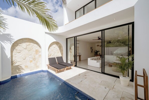 A modern outdoor pool area with stone arches, lounge chairs, and a potted plant. - Elements A6 Villa Bingin (Pecatu)