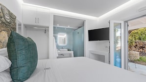 A modern bedroom with a large bed, a walk-in closet, a bathroom with a sink and mirror, and a TV mounted on the wall. - Villa K Hotel (Corfu)