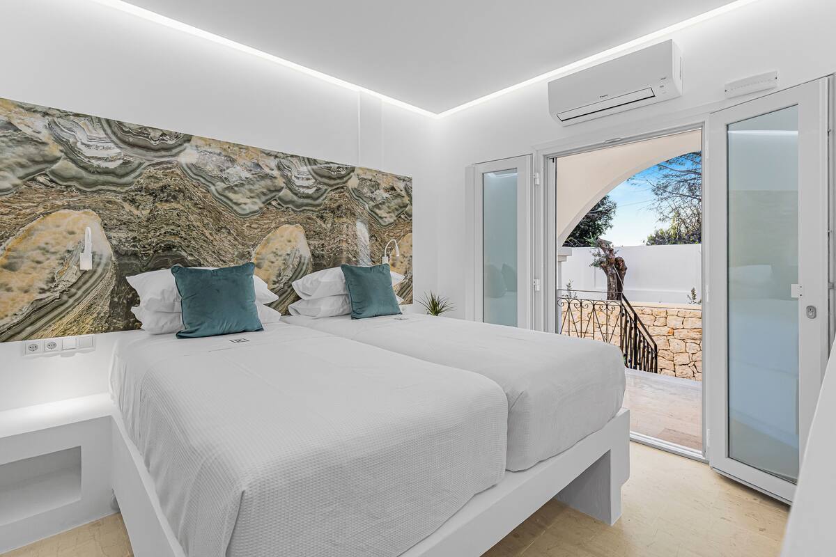 A modern bedroom with a large bed, a marble headboard, and a balcony with a stone wall.
