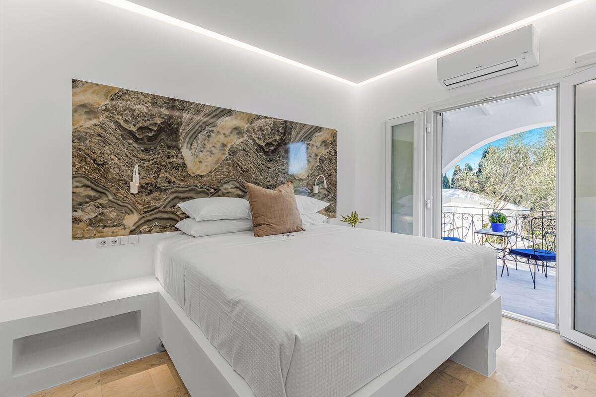 A modern bedroom with a large bed, a marble wall art piece, and a balcony with outdoor furniture.