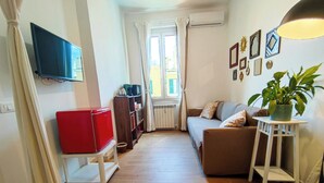 A narrow hallway with a sofa, a red refrigerator, a television, and a potted plant. - New Suite with modern living room in central area. (Roma)