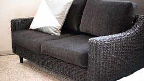 A dark wicker sofa with a white pillow and a dark cushion.