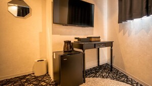 A compact hotel room with a flat-screen TV mounted above a small table, a compact refrigerator, and a trash bin.