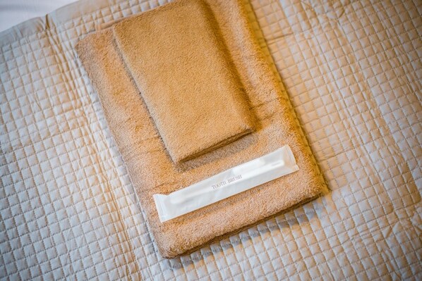 A neatly folded beige towel with a label reading "TOOTH BRUSH" on a textured, quilted surface.