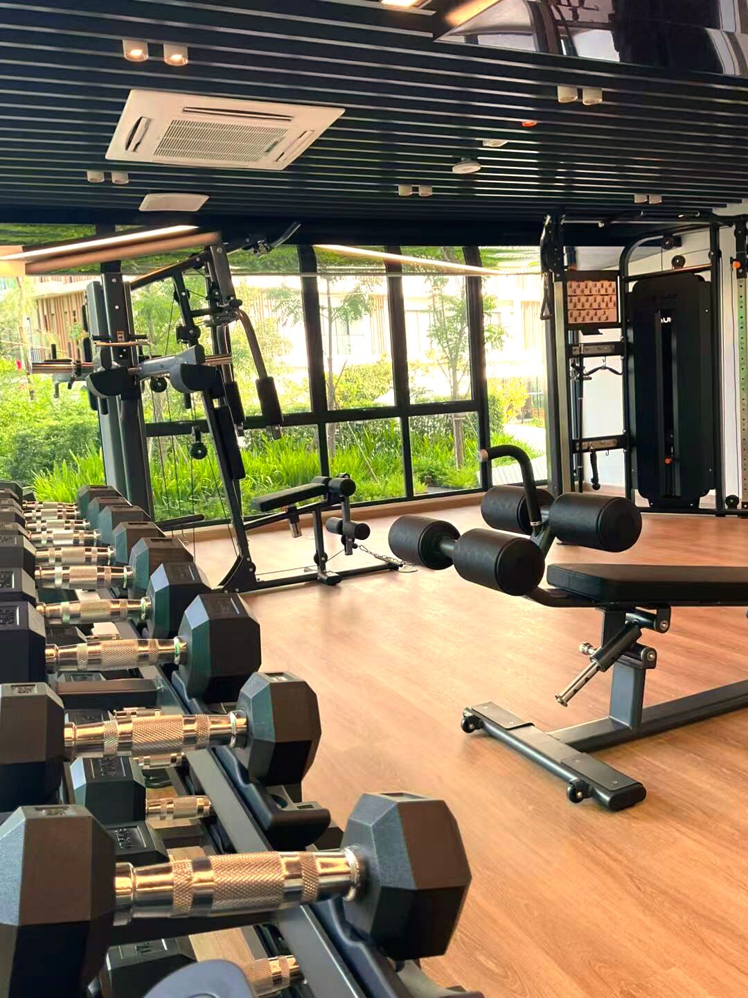 Un gimnasio con equipamiento de ejercicio, ventanas amplias y vistas a zonas verdes.