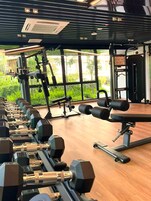 Un gimnasio con equipamiento de ejercicio, ventanas amplias y vistas a zonas verdes.