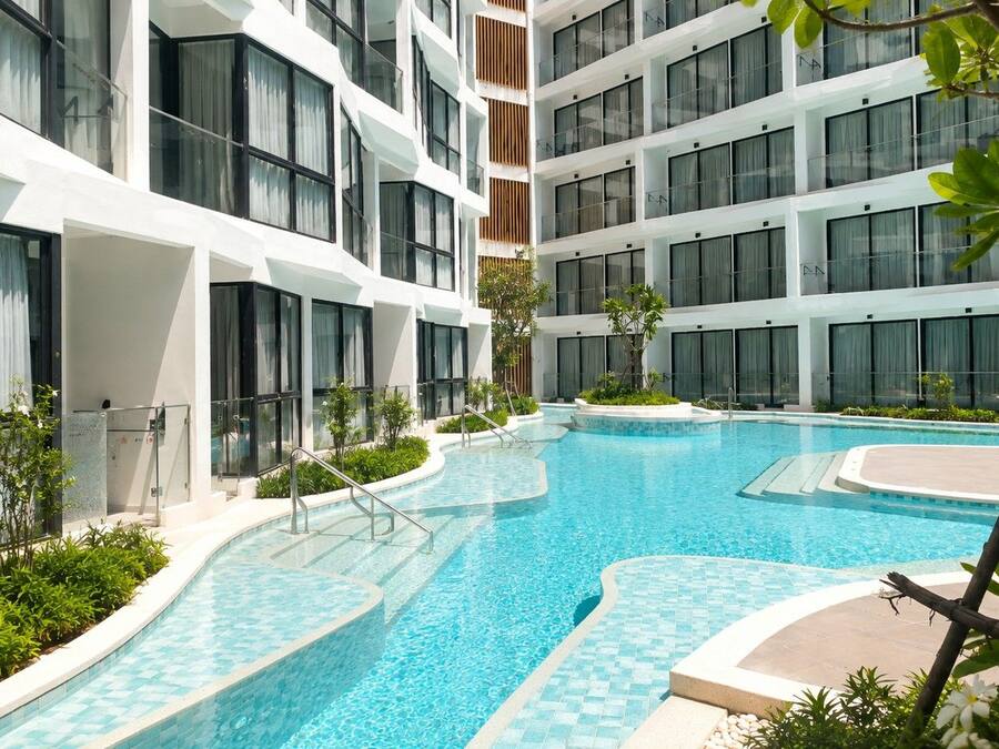 A modern hotel with a swimming pool, multiple balconies, and a well-maintained garden area.
