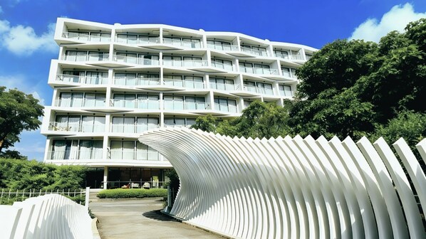 A modern multi-story hotel with balconies, a curved white structure in the foreground, and lush greenery. - Laya Suites & Residences (Choeng Thale)