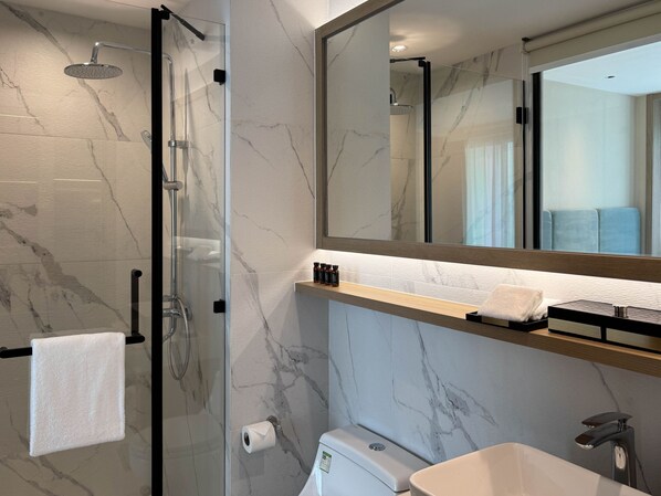 Un baño moderno con ducha envuelta en vidrio, pared con azulejos de mármol, un espejo grande, lavamanos con encimera de madera y un perchero para toallas.